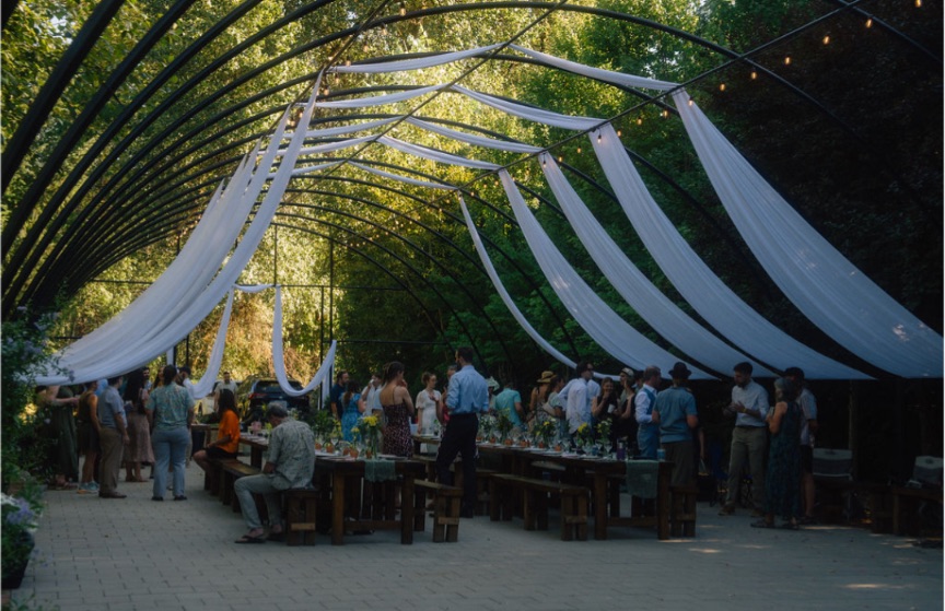 Guests gathered at long farm tables under the draped arbor at FernHaus in Gales Creek, Oregon
